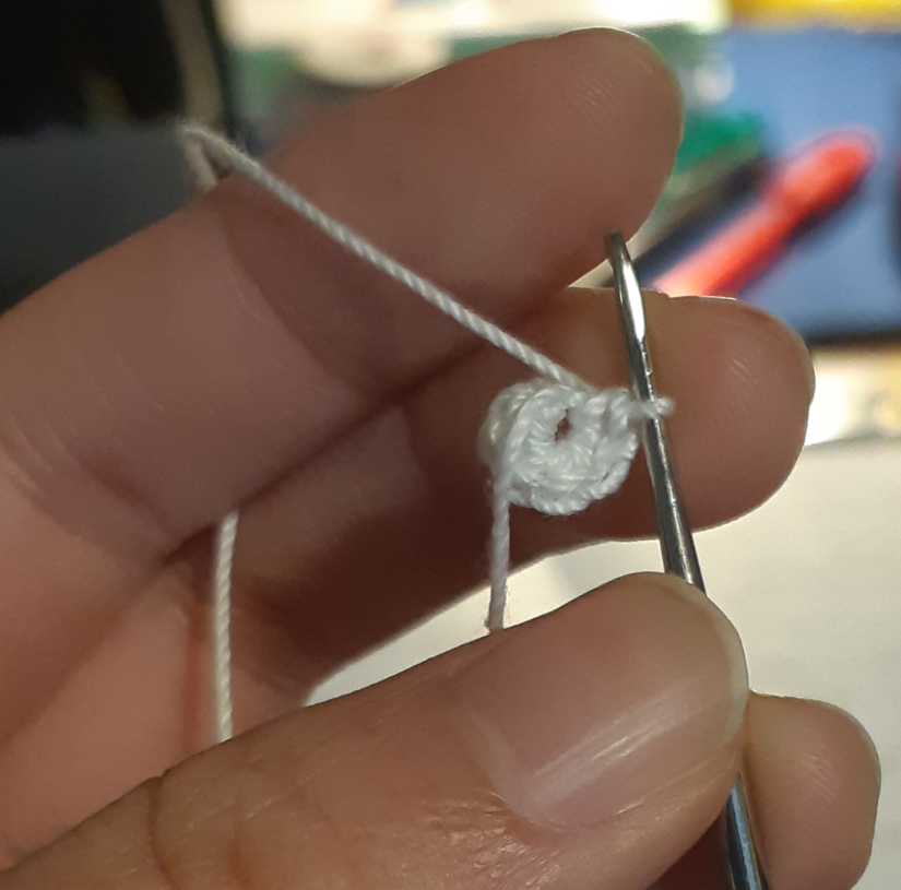 A close-up picture of the magic ring stitch, made out of size 10 crochet thread and a 1.25mm crochet hook. The size of the ring is smaller than the person's thumb.