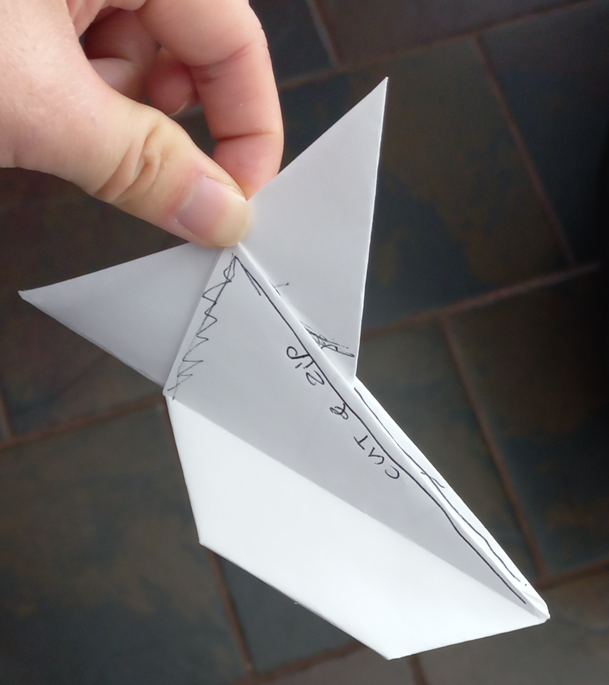 An origami balloon-style fish, folded out of paper; comments have been drawn onto the piece, to mark out places for stitching and potentially installing fasteners or zips.